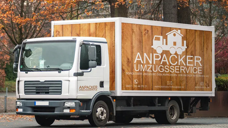 LKW mit Kofferaufbau in Holzoptik und der Aufschrift „Anpacker Umzugsservice“, dahinter Herbstbäume.