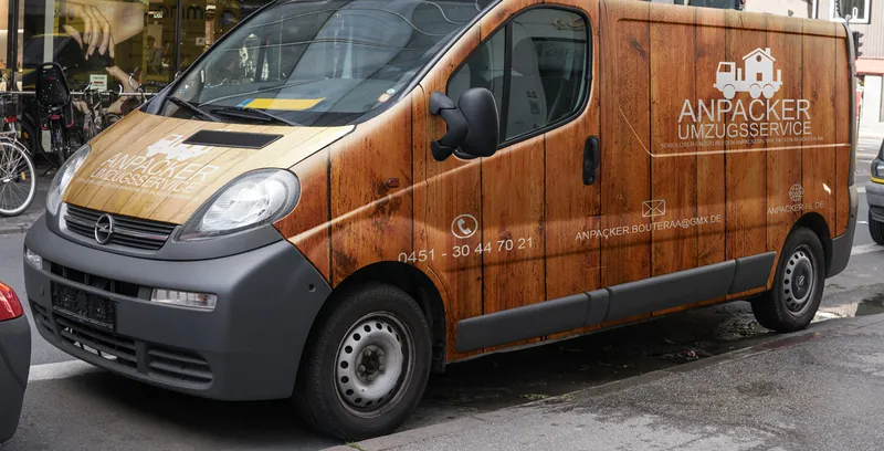 Transporter in Holzoptik mit der Aufschrift „Anpacker Umzugsservice“ und dem Bildzeichen aus LKW und Haus.